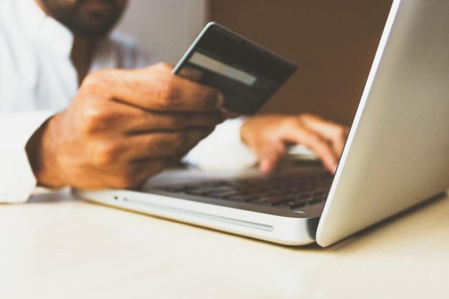 Personne tenant une carte bancaire devant un ordinateur portable lors d'un achat en ligne